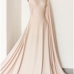 May include: A one-shoulder dress made of a soft, flowing fabric in a light beige color. The dress has a long, flowing skirt and a fitted bodice.