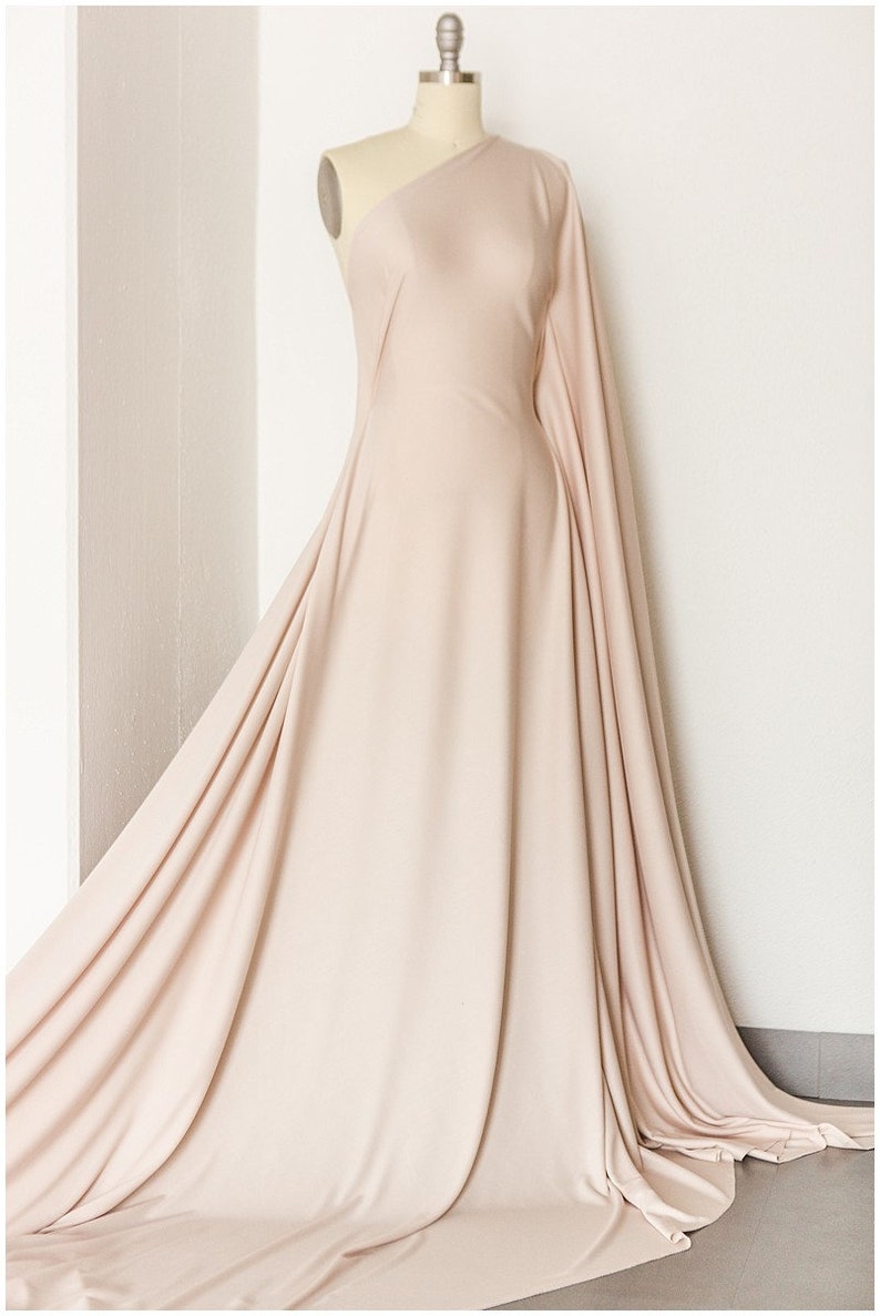 May include: A one-shoulder dress made of a soft, flowing fabric in a light beige color. The dress has a long, flowing skirt and a fitted bodice.