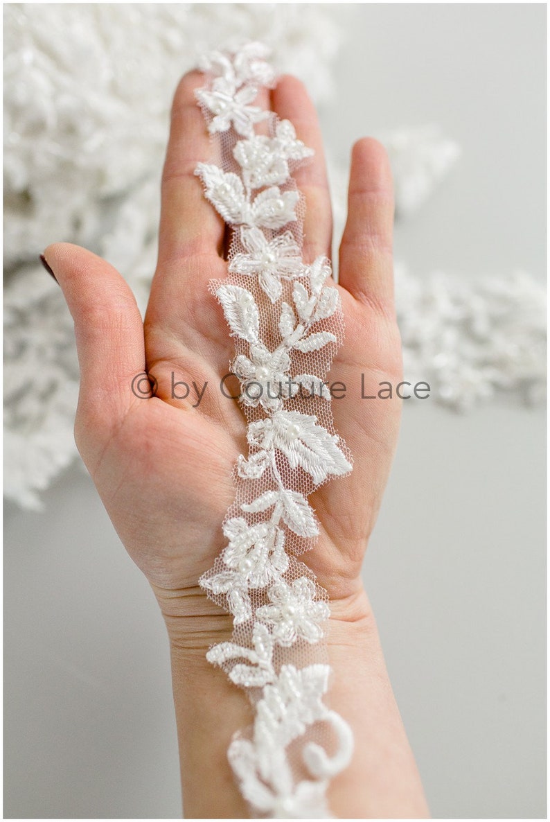 May include: White beaded lace trim with floral designs. The lace is delicate and features small pearl-like beads.