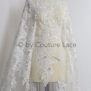 May include: White beaded lace fabric with floral designs and sequins. The fabric is draped over a dress form. The text "by Couture Lace" is visible in the image.