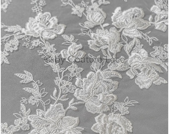 May include: White floral lace fabric with a delicate embroidered design. The lace features a repeating pattern of flowers and leaves.