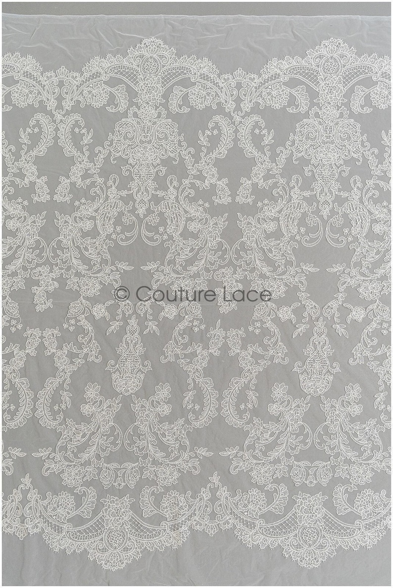 May include: White lace fabric with a delicate floral pattern. The lace has a scalloped edge and is perfect for adding a touch of elegance to any project.