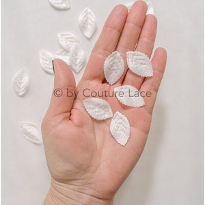 Puede incluir: Una mano sosteniendo una colección de hojas de tela blanca. Las hojas son delicadas y tienen una superficie ligeramente texturizada.  © by Couture Lace