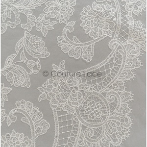 May include: White lace fabric with a delicate floral pattern. The lace is intricate and detailed, with a paisley-like design.