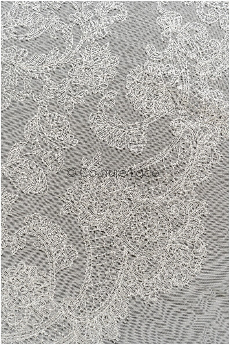 May include: White lace fabric with a delicate floral pattern. The lace is intricate and detailed, with a paisley-like design.