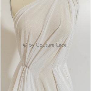 May include: White sparkly fabric draped over a dress form. The fabric is sheer and has a subtle shimmer. The text "&copy; by Couture Lace" is visible in the lower center of the image.