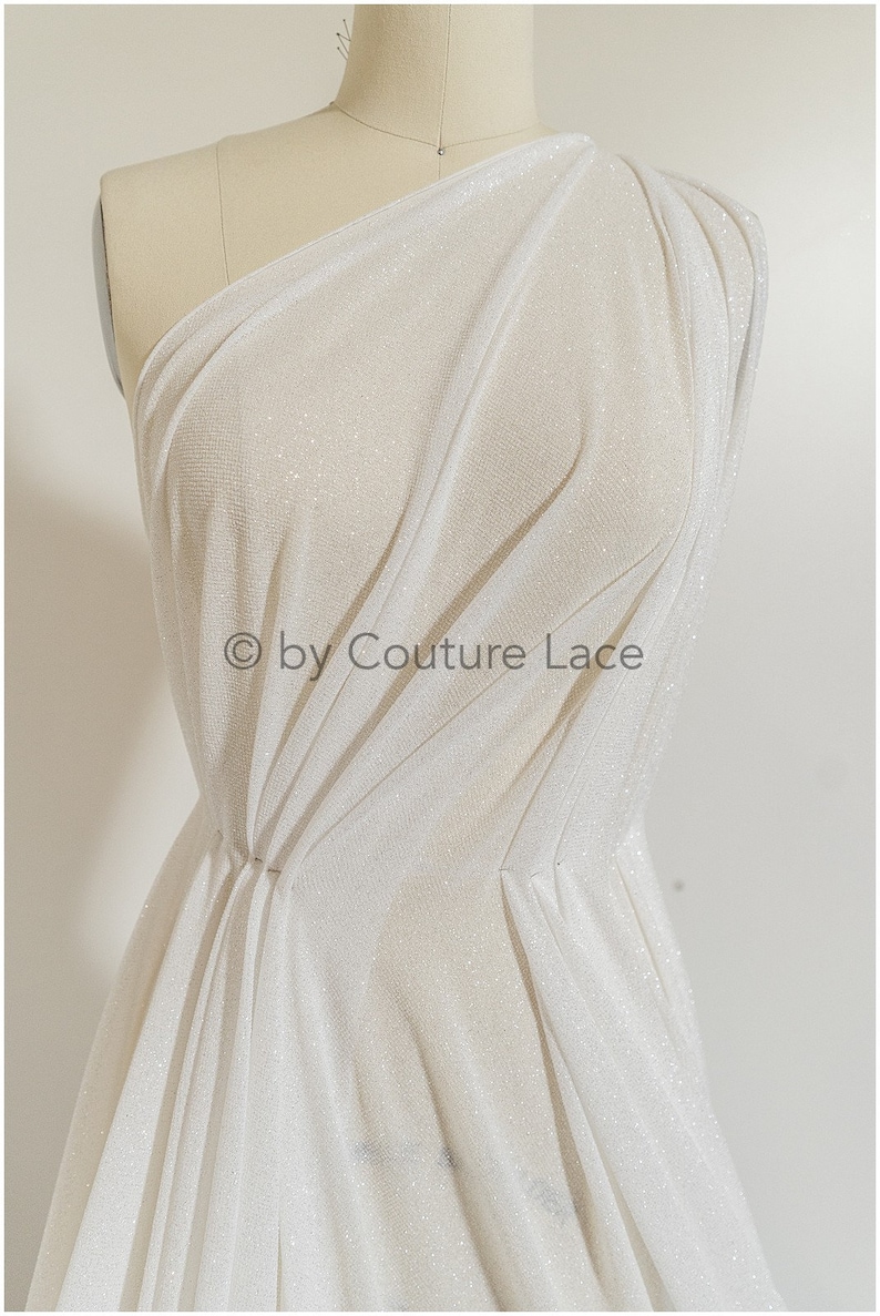 May include: White sparkly fabric draped over a dress form. The fabric is sheer and has a subtle shimmer. The text "&copy; by Couture Lace" is visible in the lower center of the image.