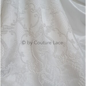 May include: White fabric with an embossed, intricate floral pattern. The fabric has a subtle sheen and a soft texture.