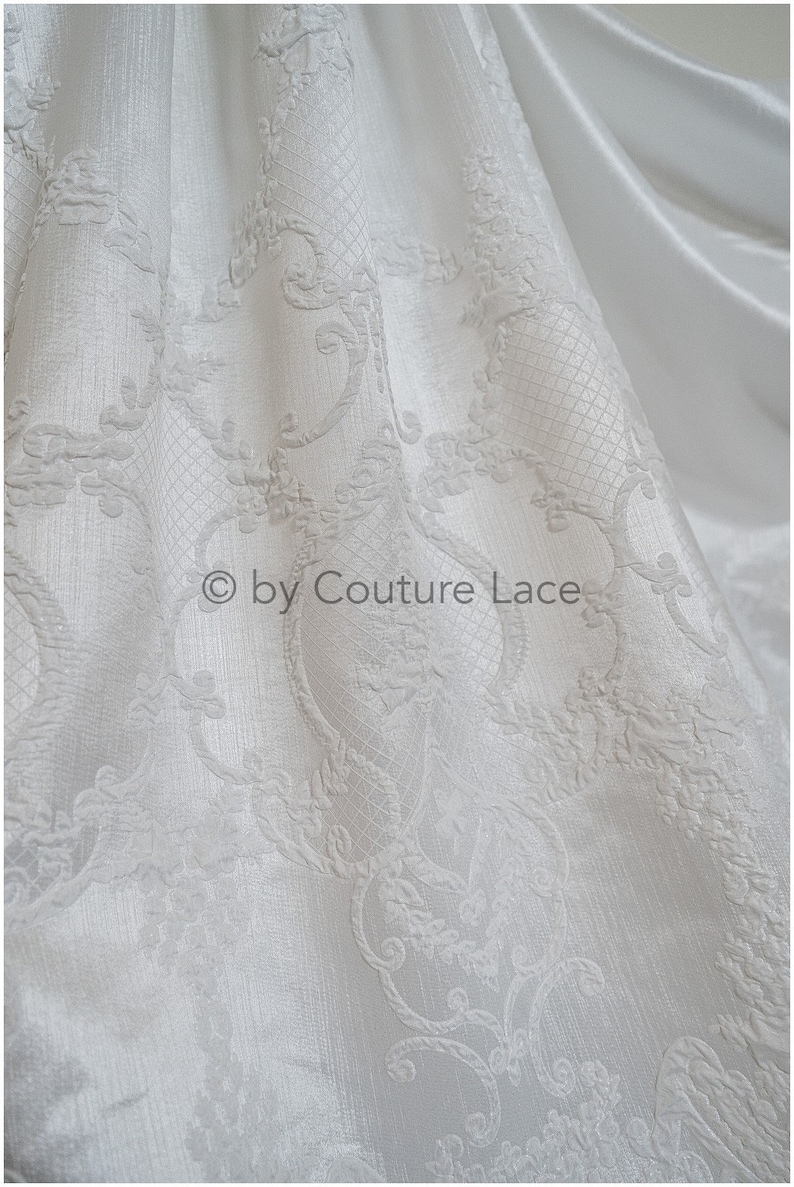 May include: White fabric with an embossed, intricate floral pattern. The fabric has a subtle sheen and a soft texture.