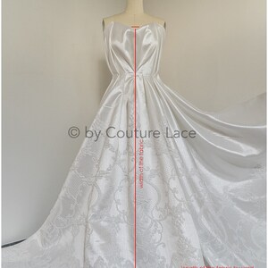 May include: White satin fabric with a damask pattern. The fabric is draped over a dress form and measured for length and width. The text "by Couture Lace" is visible in the image.