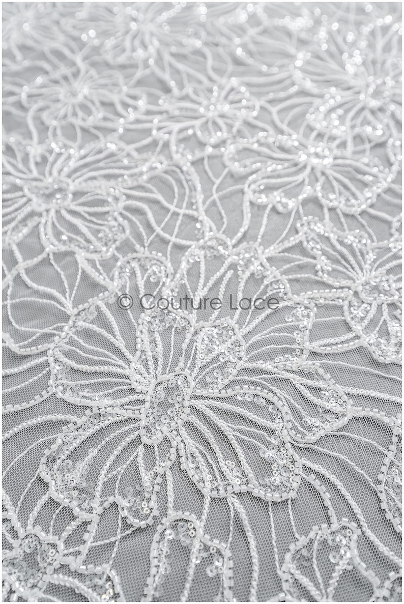 Pu&ograve; includere: Tessuto di pizzo bianco perlato con motivo floreale. Il tessuto &egrave; delicato e intricato, con piccole paillettes sparse su tutto il tessuto.