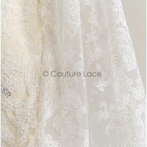 May include: White lace fabric with a delicate floral pattern. The lace is sheer and has a soft, flowing texture. &copy; Couture Lace