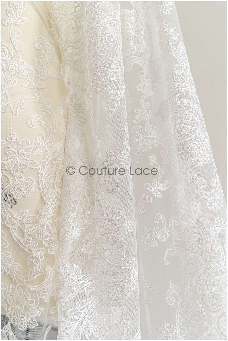 May include: White lace fabric with a delicate floral pattern. The lace is sheer and has a soft, flowing texture. &copy; Couture Lace
