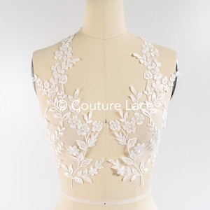 May include: White floral lace applique with delicate flowers and leaves. The lace is on a mannequin and is perfect for adding a touch of elegance to any garment.
