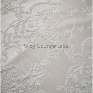 May include: White fabric with an embossed, intricate, floral pattern. The fabric has a subtle sheen and a delicate texture.