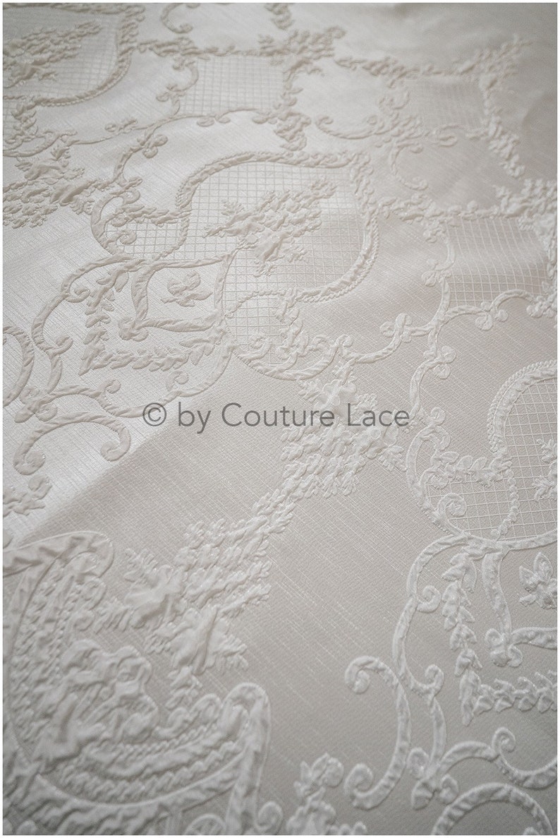 May include: White fabric with an embossed, intricate, floral pattern. The fabric has a subtle sheen and a delicate texture.