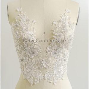 Op de afbeelding: Witte bloemenkant applique met delicate kralen. De kant is op een wit mannequin torso. De tekst "© by Couture Lace" is zichtbaar in het midden van de afbeelding.