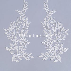 May include: Two white lace appliques with a floral design. The appliques are on a light purple background. The text "Couture Lace" is visible in the center of the image.