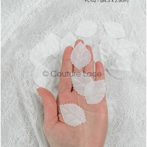 May include: White lace fabric with small white fabric leaves, approximately 4.3 by 2.9 centimetres, on a hand. The text "FL-021 (04.3 x 2.9cm)" and "Couture Lace" are visible in the image.