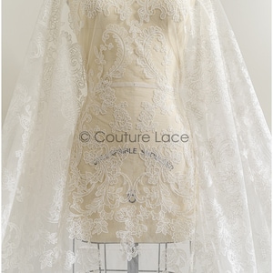 May include: White floral lace fabric with a delicate pattern. The lace is on a white mannequin and is draped over a white background. The text "Couture Lace" is visible on the fabric.