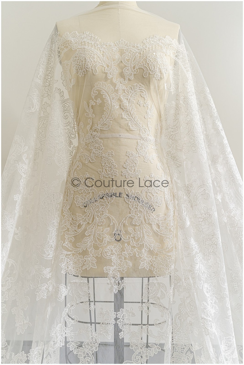 May include: White floral lace fabric with a delicate pattern. The lace is on a white mannequin and is draped over a white background. The text "Couture Lace" is visible on the fabric.