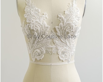 May include: A pair of white lace appliques with a floral design. The appliques are shown on a white dress form.