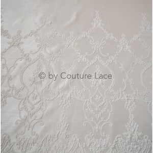 May include: White lace fabric with a delicate, embossed floral pattern. The lace has a scalloped edge and is perfect for adding a touch of elegance to any project.