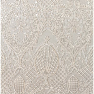 K&ouml;nnte beinhalten: Wei&szlig;er, gestickter Spitzenstoff mit einem zarten floralen und geometrischen Muster. Der Stoff hat eine weiche, flie&szlig;ende Textur und ist perfekt f&uuml;r die Herstellung eleganter Kleidungsst&uuml;cke oder Wohnaccessoires.