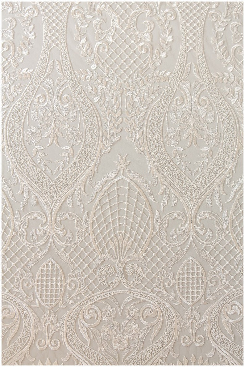 K&ouml;nnte beinhalten: Wei&szlig;er, gestickter Spitzenstoff mit einem zarten floralen und geometrischen Muster. Der Stoff hat eine weiche, flie&szlig;ende Textur und ist perfekt f&uuml;r die Herstellung eleganter Kleidungsst&uuml;cke oder Wohnaccessoires.