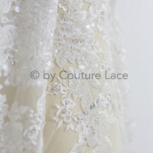 May include: White lace fabric with floral embroidery and sequins. The lace is delicate and intricate, with a soft, flowing texture. The fabric is perfect for adding a touch of elegance to any project.