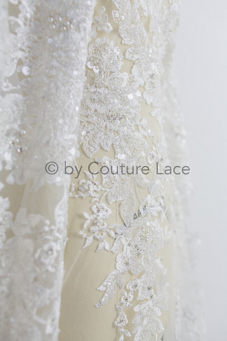 May include: White lace fabric with floral embroidery and sequins. The lace is delicate and intricate, with a soft, flowing texture. The fabric is perfect for adding a touch of elegance to any project.