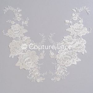 Puede incluir: Aplique de encaje blanco con un diseño floral. El aplique presenta flores y hojas delicadas, creando un look romántico y elegante.