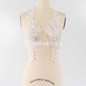 Puede incluir: Aplique de encaje blanco con un diseño de hojas, mostrado en un maniquí. El aplique está hecho de encaje delicado y presenta un patrón floral. El aplique es perfecto para agregar un toque de elegancia a cualquier prenda.