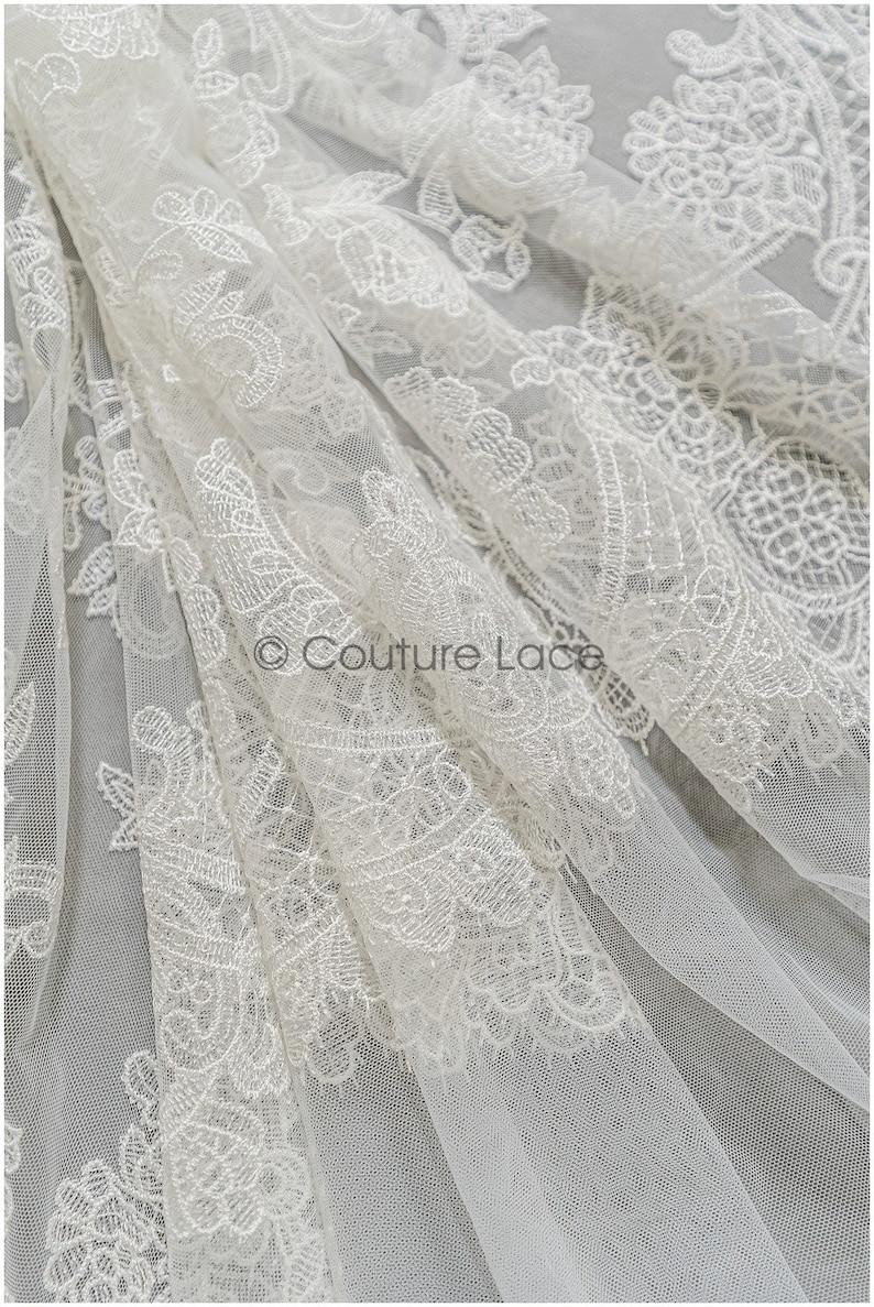 May include: White floral lace fabric with a delicate pattern. The lace is sheer and has a soft, flowing texture.  &copy; Couture Lace