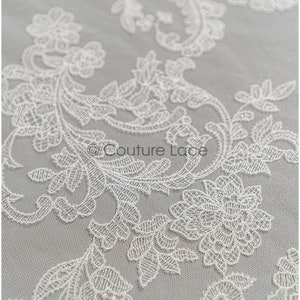 May include: White floral lace fabric with a delicate pattern. The lace is on a sheer mesh background.
