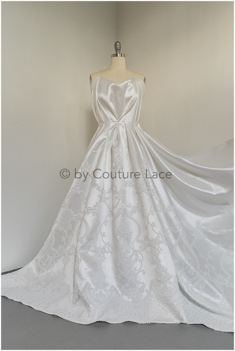 May include: A white strapless wedding dress with a fitted bodice and a flowing skirt. The skirt features a delicate floral pattern.