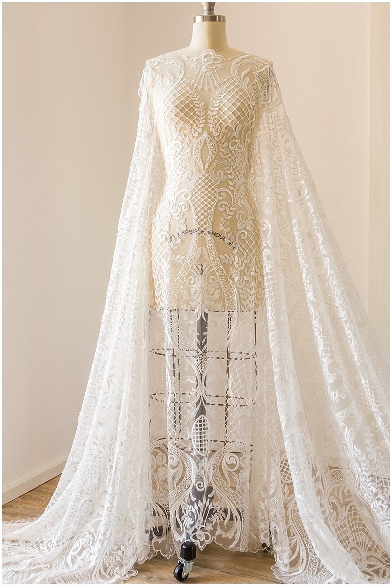 K&ouml;nnte beinhalten: Wei&szlig;er Spitzenstoff mit einem zarten Blumenmuster. Der Stoff ist &uuml;ber eine Kleiderpuppe drapiert und hat einen flie&szlig;enden, &auml;therischen Look.