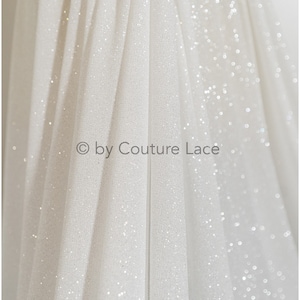 May include: White tulle fabric with a subtle sparkle. The fabric is folded and draped, creating a soft, flowing look. &copy; by Couture Lace