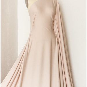 May include: A pale pink fabric draped over a dress form. The fabric is smooth and has a slight sheen. The fabric is gathered at the shoulders and flows down to the floor.