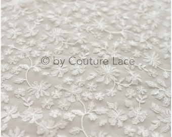 May include: White floral lace fabric with a delicate pattern. The lace is sheer and has a soft, flowing texture.