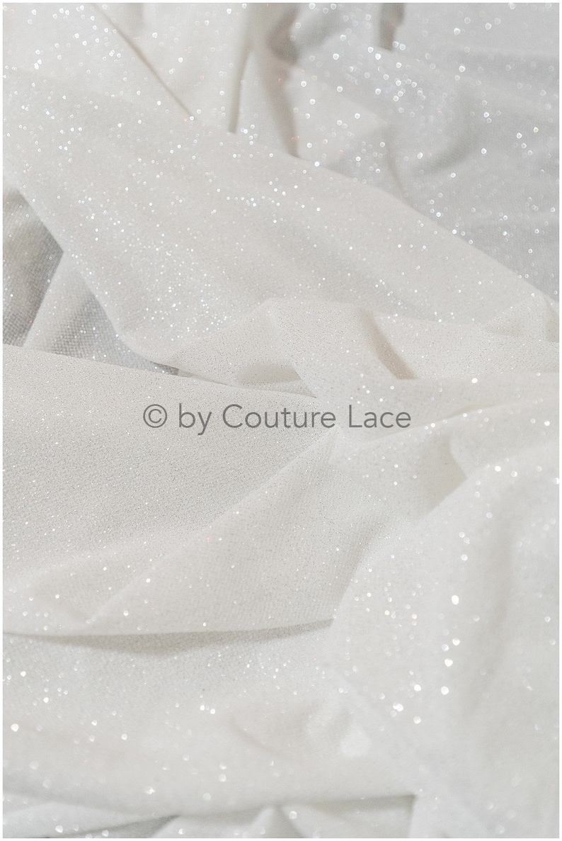 May include: White tulle fabric with a sparkly finish. The fabric is soft and sheer, with a delicate texture. &copy; by Couture Lace