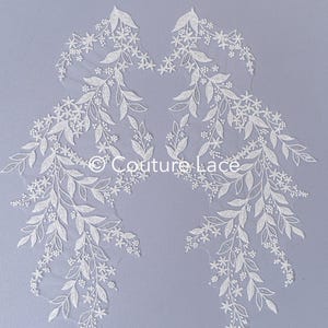May include: Two white lace appliques with floral designs. The appliques feature delicate leaves and small flowers. The appliques are perfect for adding a touch of elegance to any project.
