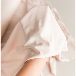 May include: A close-up of a soft, light pink fabric draped over a hand. The fabric is smooth and silky, with a subtle sheen.