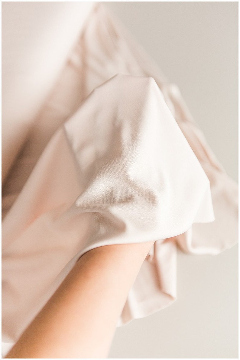 May include: A close-up of a soft, light pink fabric draped over a hand. The fabric is smooth and silky, with a subtle sheen.