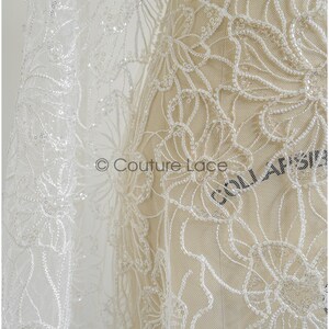 Pu&ograve; includere: Tessuto di pizzo bianco perlato con motivo floreale. Il pizzo &egrave; delicato e intricato, con piccole perline sparse su tutto il tessuto. Il tessuto &egrave; mostrato su un manichino, e il testo "Couture Lace" &egrave; visibile nell'angolo inferiore sinistro.