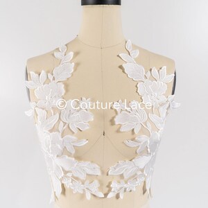 May include: White floral lace applique with delicate leaves and flowers. The lace is shown on a white dress form.