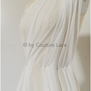 May include: White sheer fabric with a sparkly finish. The fabric is draped over a dress form and has a slight sheen. The fabric is lightweight and has a soft texture. &copy; by Couture Lace