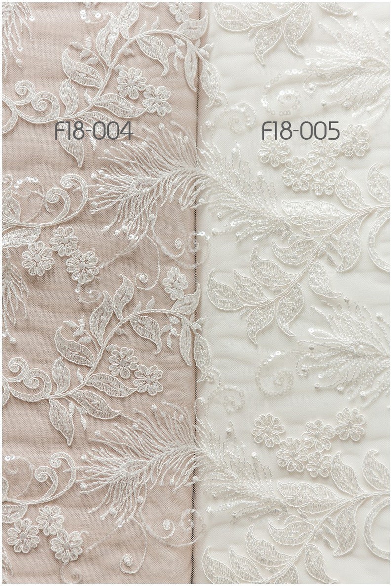 May include: Two samples of white lace fabric with a floral and feather design. The fabric on the left is a light beige color and the fabric on the right is white. The fabric on the left is labeled "F18-004" and the fabric on the right is labeled "F18-005".
