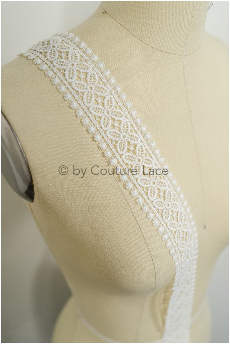 Puede incluir: Borde de encaje blanco con borde festoneado y un delicado patr&oacute;n floral.  "&copy; by Couture Lace" est&aacute; impreso en el borde.