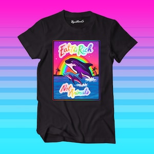 Può includere: Maglietta nera con una grafica di due delfini che saltano fuori dall'acqua con un arcobaleno dietro di loro. Il testo "Eat the Rich Not Animals" è scritto in un font arcobaleno.